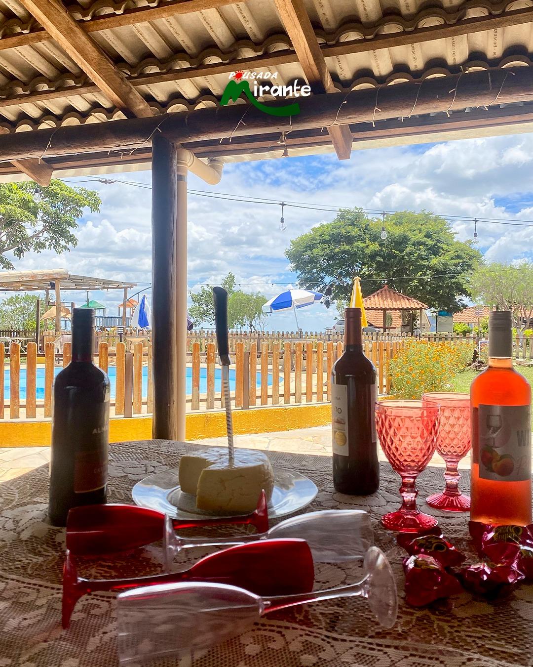 Mesa com queijo canastra, vinhos e taças vermelhas ao lado da piscina